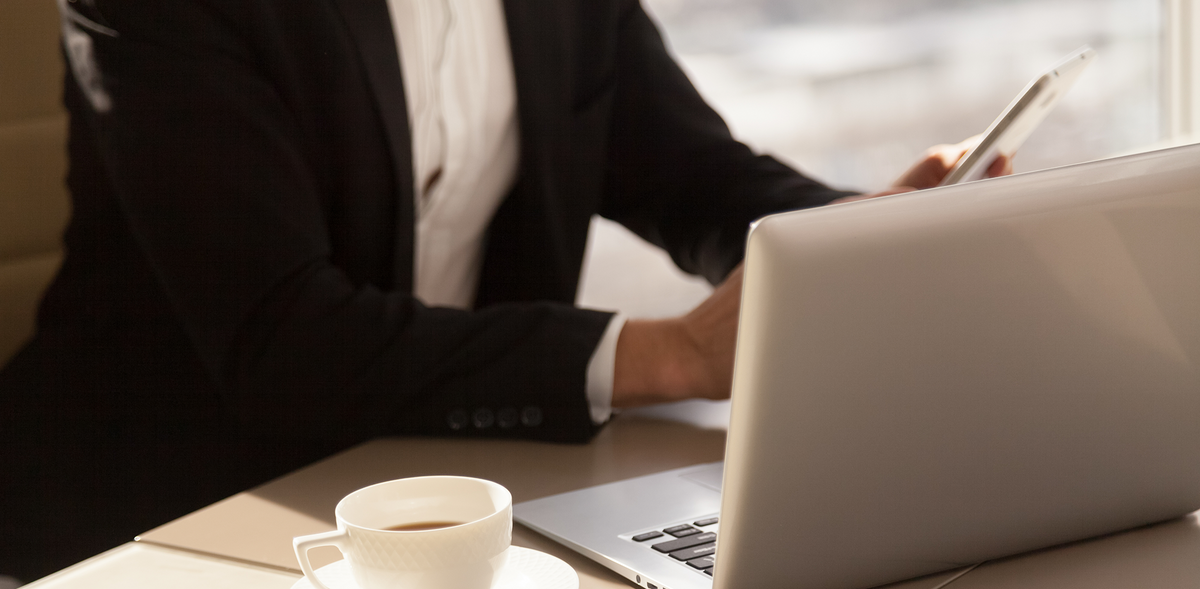 Businessperson in a suit checking a smartphone at a desk with an LG laptop