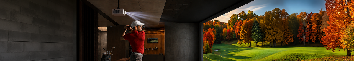 A man swings a golf club in an indoor simulator room lit by a ceiling-mounted LG projector displaying an autumn golf course