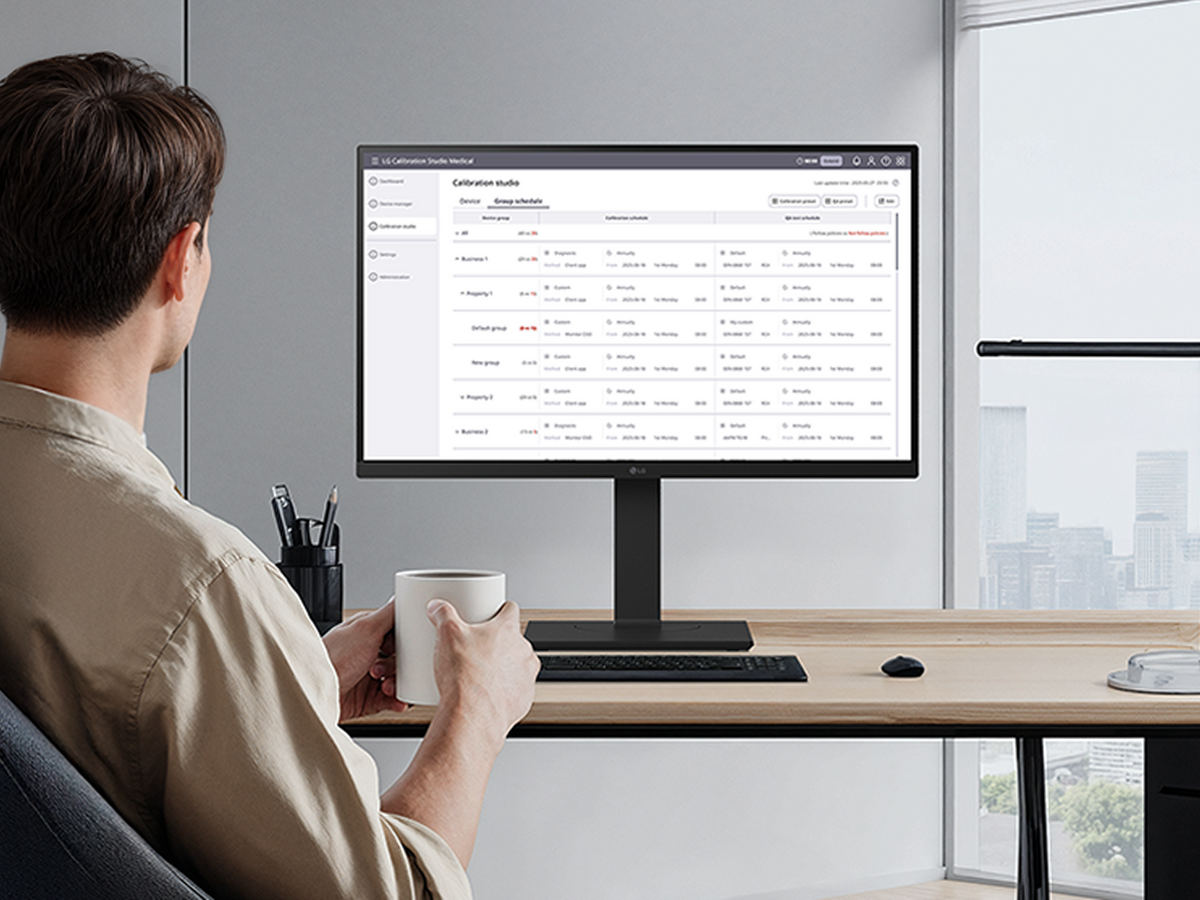 A man holding a mug while viewing the LG Calibration Studio dashboard on a computer screen.   