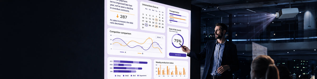 A man in a suit points at data charts projected onto a screen by a ceiling-mounted projector in a darkened room, with an audience member seated in the foreground.
